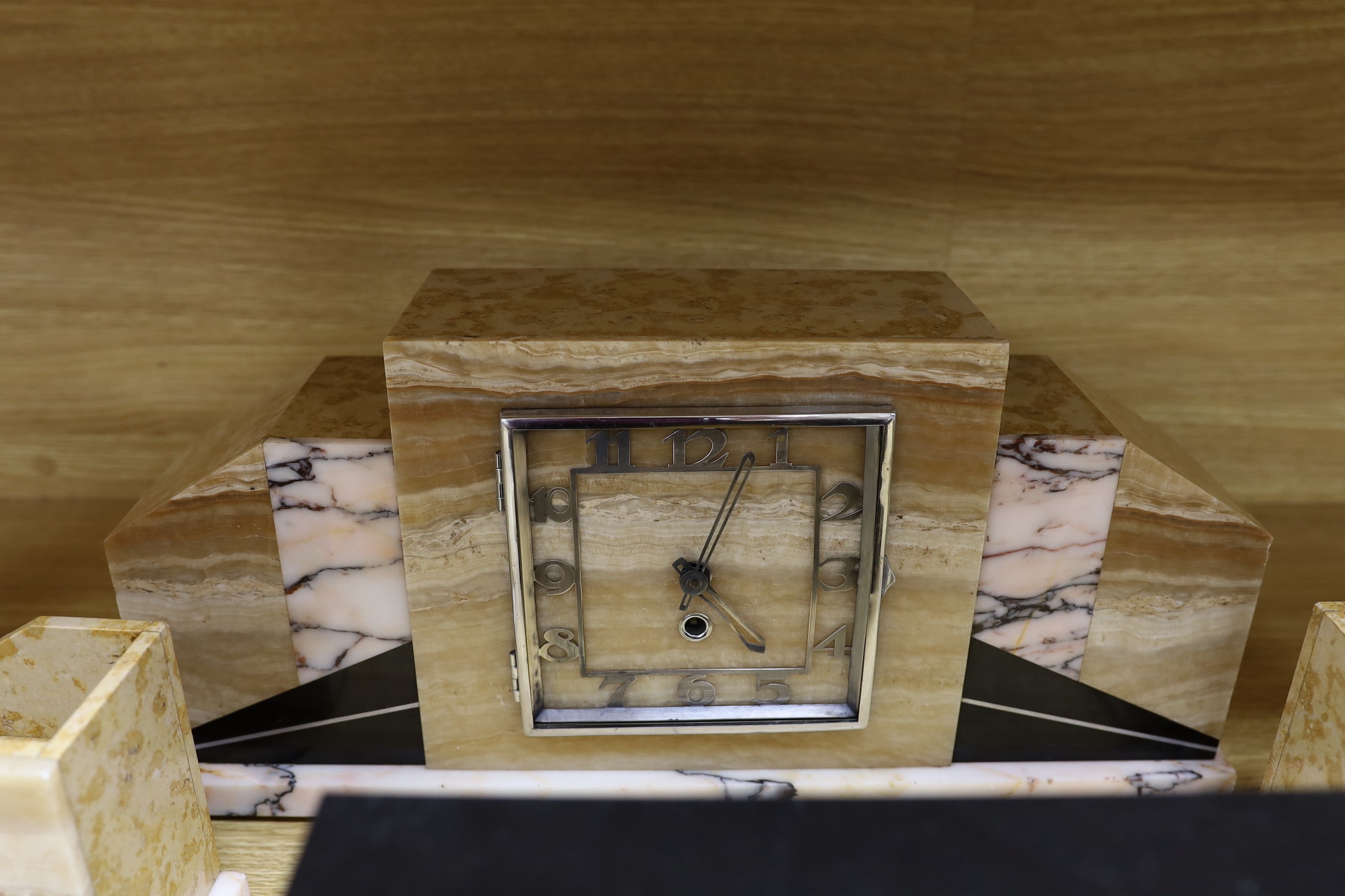 An Art Deco marble and onyx clock garniture, together with another stylised onyx Art Deco marble clock garniture with decorative silver-coloured reliefs
